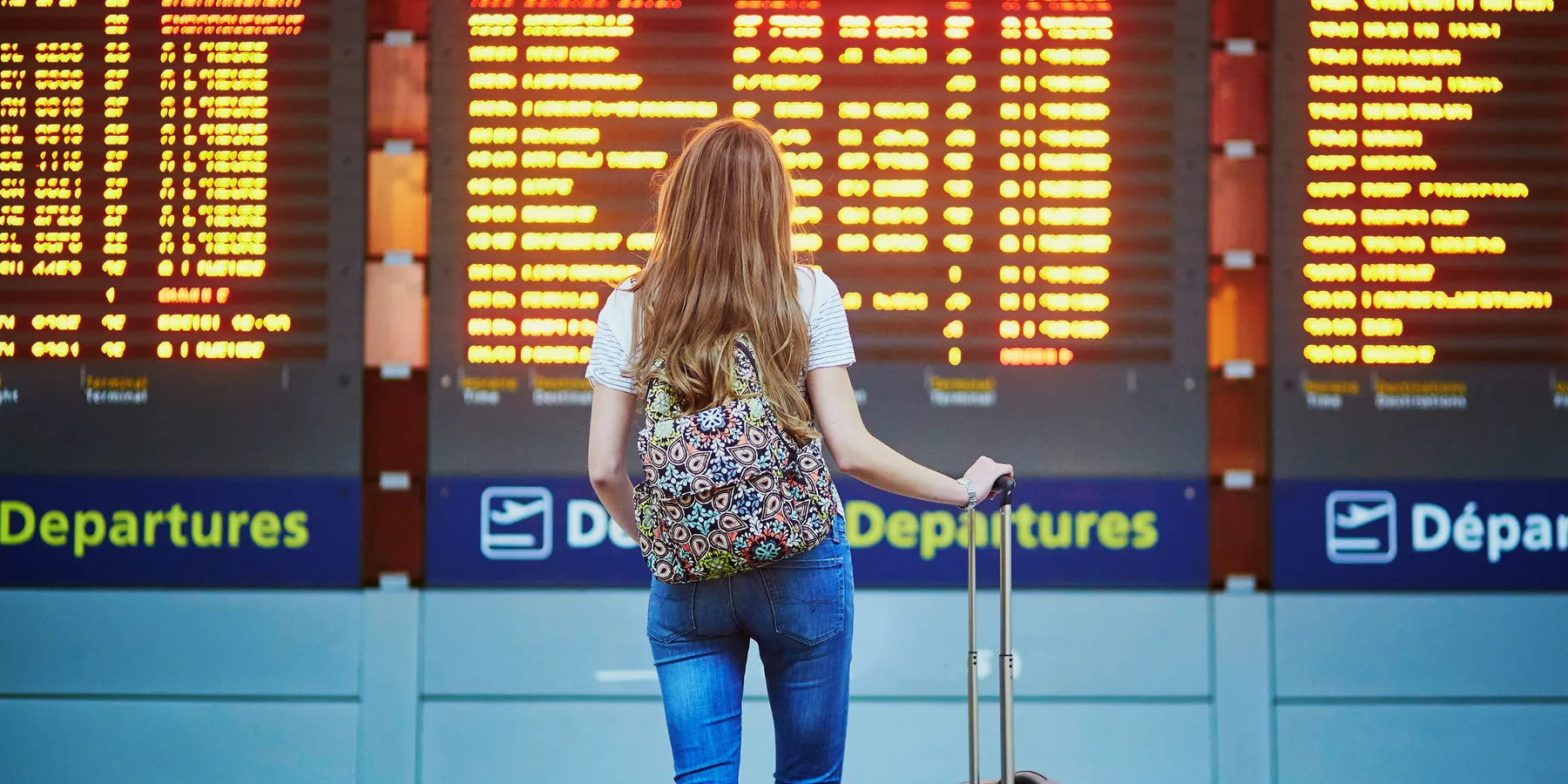 Traveller with suitcase looking at airport departures boards